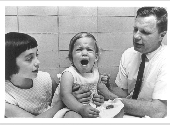 El Dr. Robert Weibel vacuna a la hija de Maurice Hilleman contra las paperas, mientras observa a su media hermana, Jeryl Lynn.